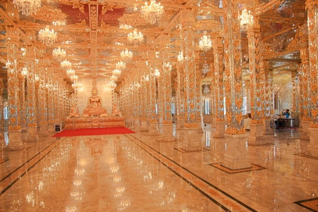 ภายในพระวิหารประดับกระจกและสีทองระยิบระยับ มีเสาเรียงรายและโคมไฟหรู พร้อมพระพุทธรูปด้านหน้า