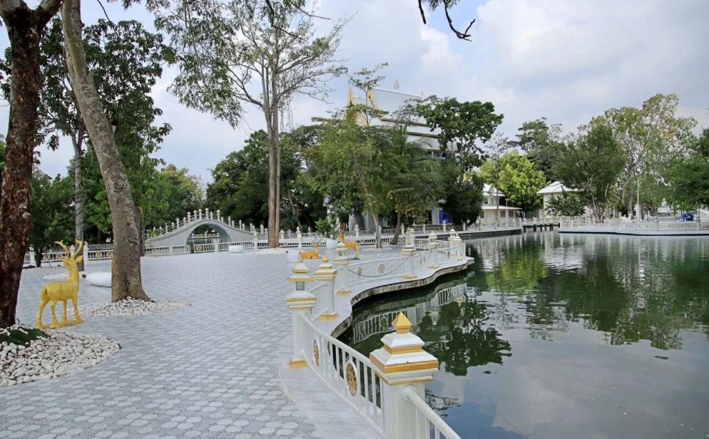 ทางเดินรอบสระน้ำภายในวัด มีรั้วสีขาวและรูปปั้นกวางสีทอง พร้อมสะพานโค้งด้านหลัง