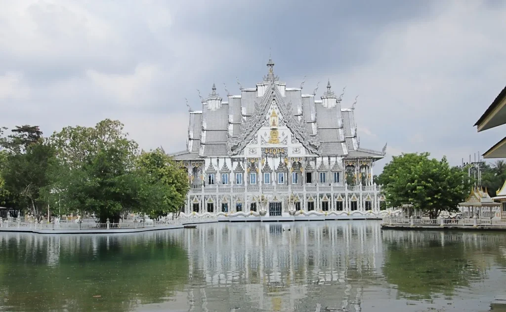 ด้านหน้าวิหารสีขาวสะท้อนน้ำในสระ บรรยากาศเงียบสงบ ล้อมรอบด้วยต้นไม้และรั้วสีขาว