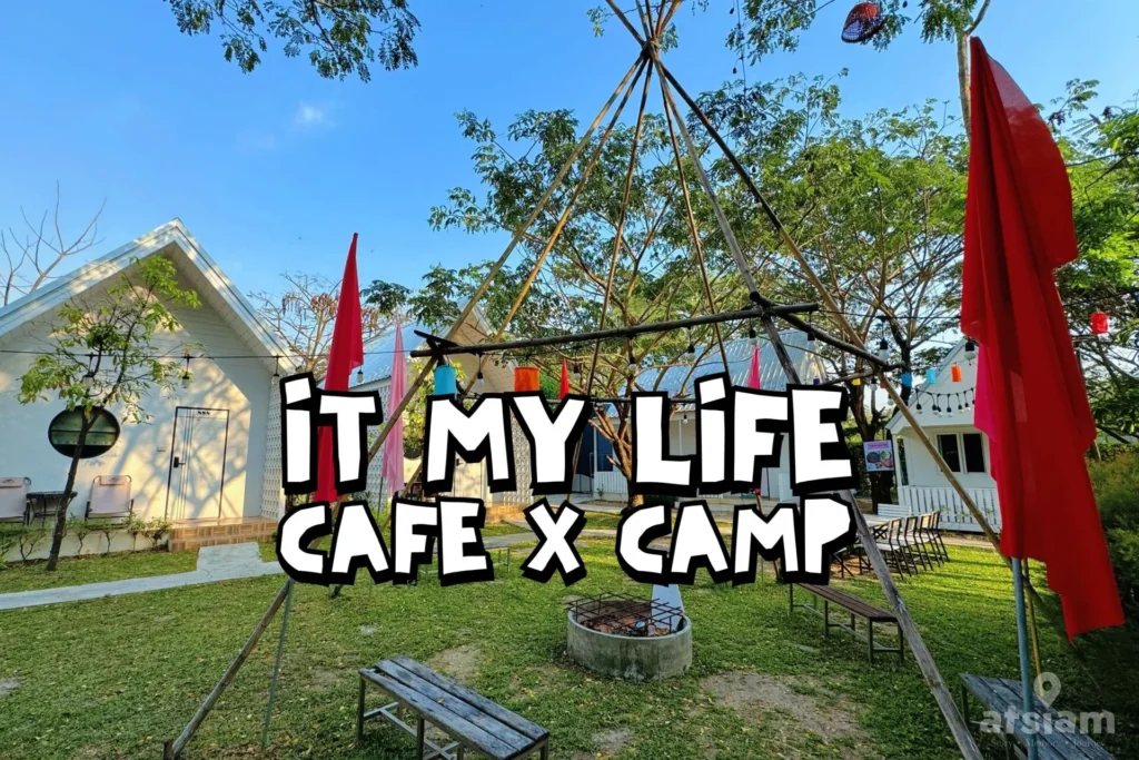 บรรยากาศลานกิจกรรมและที่พักสไตล์แคมป์ของ It My Life Cafe X Camp บางพระ ศรีราชา รายล้อมด้วยต้นไม้และบ้านพักสีขาว