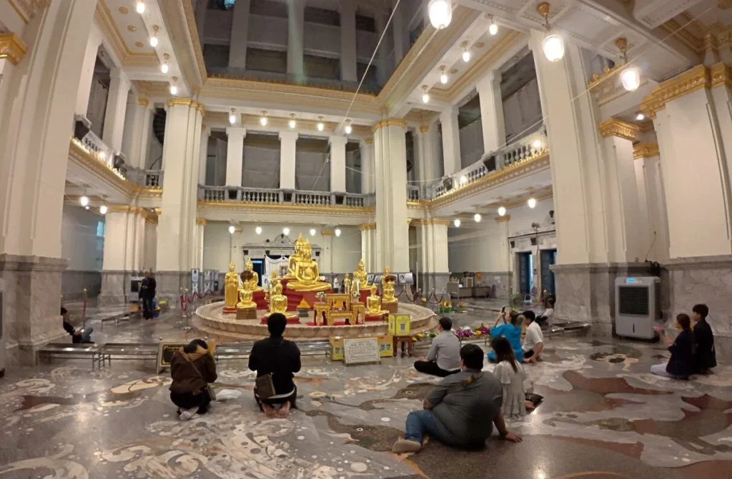 ภายในโถงวัด มีพระพุทธรูปหลายองค์และผู้คนกำลังกราบไหว้