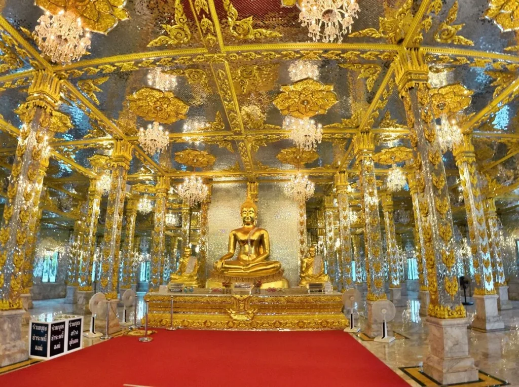 พระพุทธรูปสีทองประดิษฐานบนแท่น ภายในวิหารที่ตกแต่งกระจกและลวดลายสีทองสวยงาม